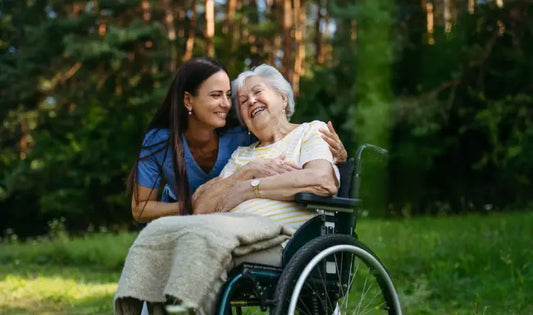 Healthcare worker providing compassionate care and communication support to an elderly woman in a wheelchair outdoors