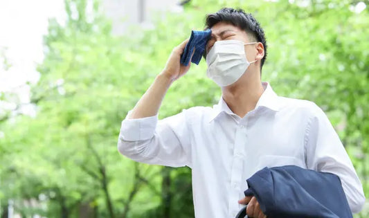 Heat stress awareness training showing an office worker wearing a face mask wiping sweat from his forehead outdoors during hot weather.