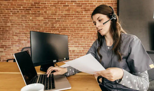 Administrative support assistant reviewing documents while using a laptop and wearing a headset in an office