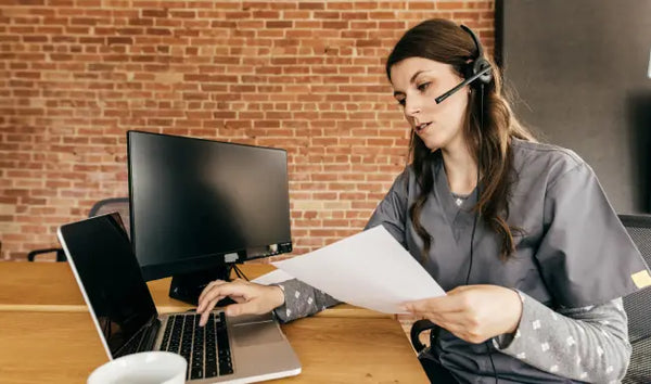 Administrative support assistant reviewing documents while using a laptop and wearing a headset in an office