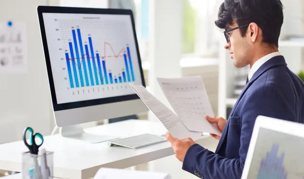 Business analyst reviewing financial reports and performance charts on a desktop computer in a modern office
