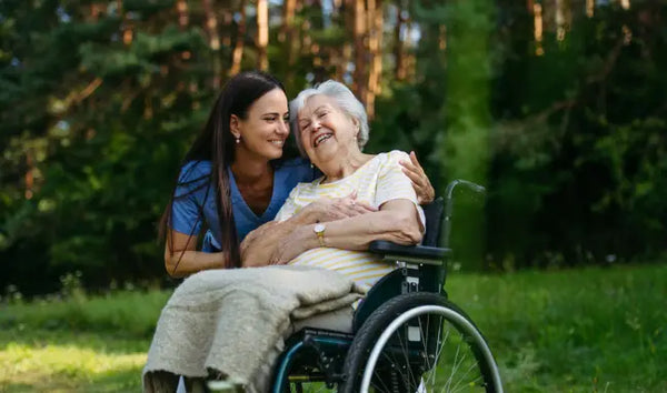 Healthcare worker providing compassionate care and communication support to an elderly woman in a wheelchair outdoors