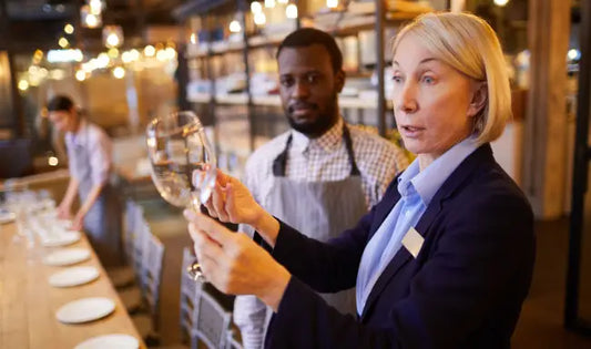 Food and beverage manager inspecting a wine glass while supervising restaurant service and hospitality operations.