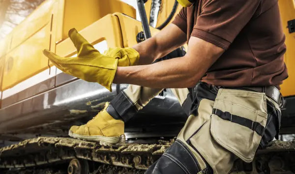 Construction worker wearing protective gloves and PPE during heavy equipment safety training at an industrial worksite.