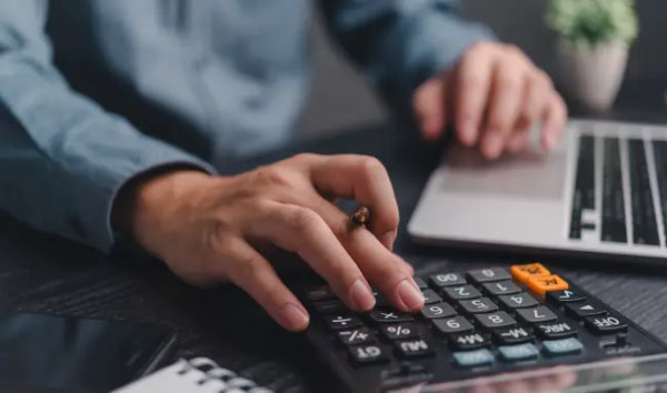 Payroll Management professional calculating employee payroll and financial records using a calculator and laptop